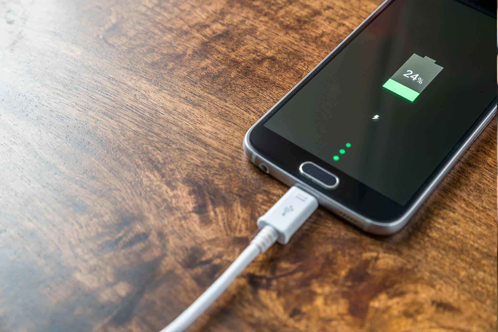  A smartphone is plugged into a fast charger with a green battery icon indicating it is charging.